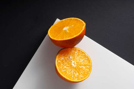 selective focus, juicy orange halves on a white square corner, on a black paper backgroundの写真素材