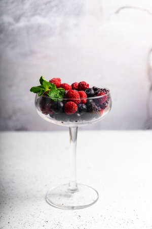 frozen blueberries, raspberries and blackberries on a light textured background. in a tall...