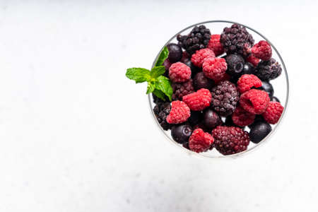 frozen blueberries, raspberries and blackberries on a light textured background. in a tall...