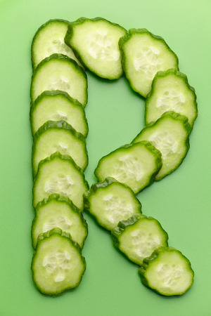 R letter made of raw cucumber on green backgroundの写真素材