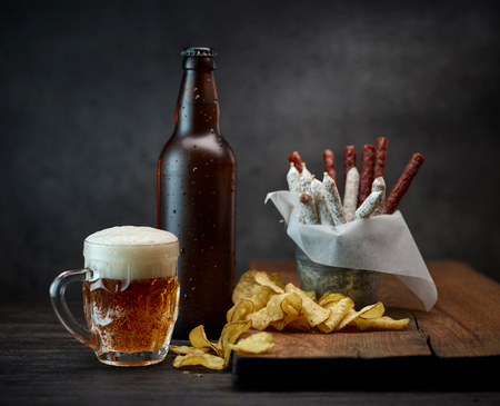 beer mug, bottle and snacks on dark wooden tableの写真素材