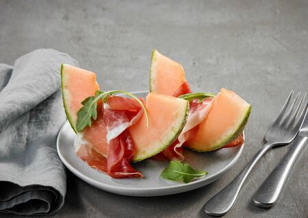 plate of melon and prosciutto ham on grey kitchen tableの写真素材