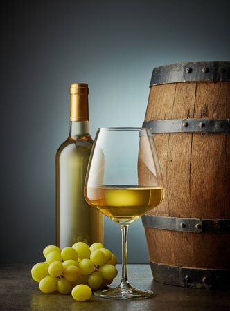 glass and bottle of white wine and old wooden barrelの写真素材