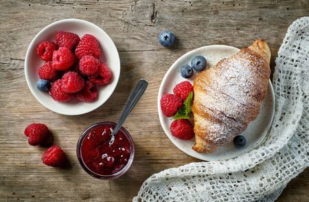 sweet croissant and berries on old wooden kitchen table, top viewの写真素材