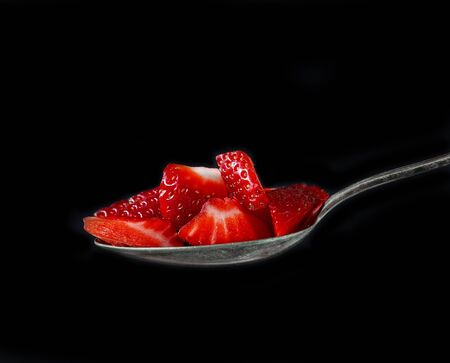spoon of strawberry pieces on black backgroundの写真素材