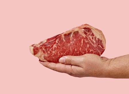 fresh raw steak in human hand isolated on pink backgroundの写真素材