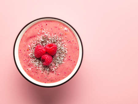 decorated breakfast smoothie bowl of banana and raspberries on pink background, top viewの写真素材