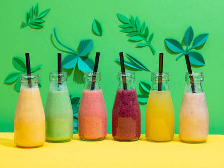 bottles of various colorful banana and berry smoothies on green paper leaf backgroundの写真素材