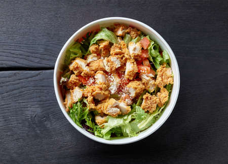 fresh caesar salad with fried chicken meat in paper take away container on black wooden table, top viewの写真素材