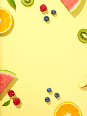 various fresh fruit slices and berries on yellow background, top viewの写真素材
