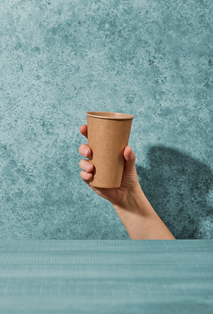 paper take away coffee cup in human hand on blue backgroundの写真素材