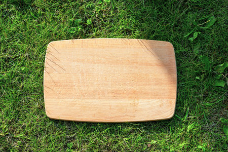 empty wooden cutting board on green grass background, top view. natural vegan eating conceptの写真素材