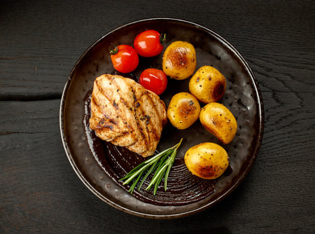 plate of freshly grilled pork fillet steak and vegetables on black wooden table, top viewの写真素材