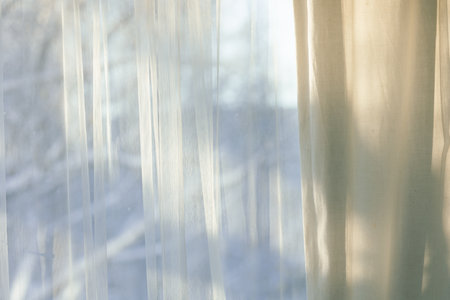 curtains hang in front of sunny winter windowの写真素材