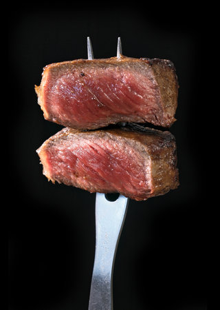 Freshly grilled pieces of beef steak meat on a fork isolated on a black background. Close-up of foodの写真素材