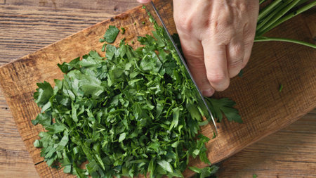 Chef chops fresh green parsley leaves on wooden cutting board to prepare healthy food, top view. Food close upの写真素材
