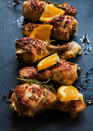 Roasted chicken legs, oranges and rosemary on the black background. Cooked with sauce from mustard, orange, honey and olive oil.の写真素材
