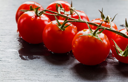 Small cherry tomatoes on black stone background. Closeup, selective focus.の写真素材