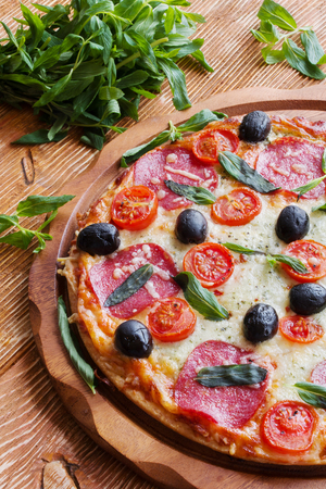 Pizza with salami, black olives and tomatoes on the wooden table.の写真素材