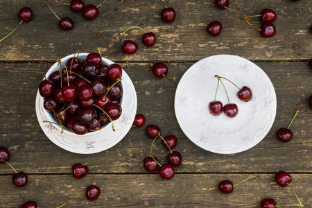 Fresh cherries in white vintage bowl on old wooden table. Ripe berries on background, summer day. Top view.の写真素材