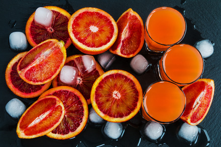 Sliced Sicilian red oranges and orange juice in small glasses on black stone background. Top view.の写真素材