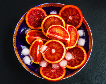 Sliced Sicilian red oranges on dark-blue plate. Black stone background, top view.の写真素材