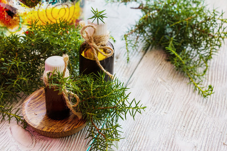Juniper essential oil in a glass bottle on a wooden table. Used in medicine, cosmetics and aromatherapy. Fresh green sprigs. Selective focus.の写真素材