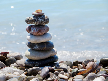 Pyramid of large pebbles with shell on top on the beach. The sea is the background, sunny day.の写真素材