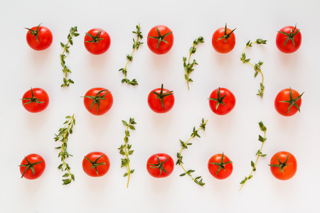Small red cherry tomatoes and fresh green thyme leaves on white table. Flat lay, top view.