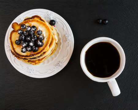 Homemade pancakes and black currant, vintage white crockery, cup of coffee, black stone background, top view.の写真素材