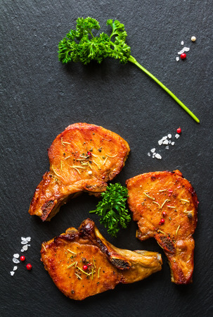 Roasted pork steaks, cutlets with bones  and fresh parsley on black stone background, top view.の写真素材
