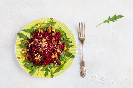 Salad with baked beets, arugula, raisins and walnuts on a green plate with vintage fork on the table in kitchen. Food background with copy space, top view, flat lay.の写真素材