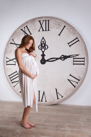 Young beautiful pregnant woman on a white background with clocの写真素材
