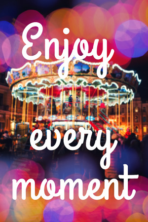 ENJOY EVERY MOMENT. Inspirational Typographic Quote. Merry-Go-Round illuminated at night with colorful bokehの写真素材