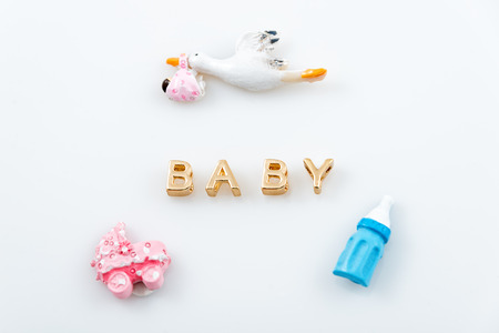 Golden letters. Word baby on white with tiny toys. Pacifier, pram and bird carrying a newborn