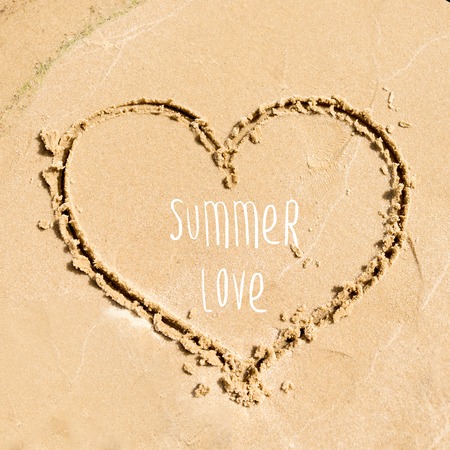 Summer time greeting card design. Shape of the heart drawn in the sand on the beachの写真素材