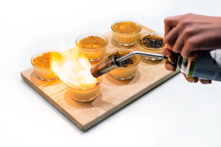 Woman's hands making creme brulee with gas-burner on wooden tray. Traditional French vanilla cream dessert with caramelised sugar on topの写真素材