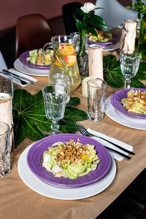 Fresh salad with chicken meat, oranges, walnuts, greens and herbs and olive oil on a decorated table...
