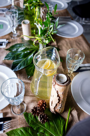 A carafe of fruity beverage with rosemary and lemon on a decorated table ready for dinner. Beautifully decorated table set for wedding or another event in the restaurantの写真素材