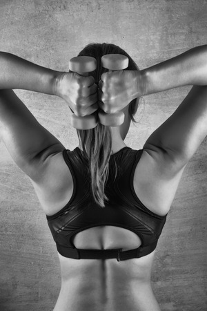 Fit woman exercising with weights on the background of a concrete wall in the gym. Healthy lifestyle conceptの写真素材