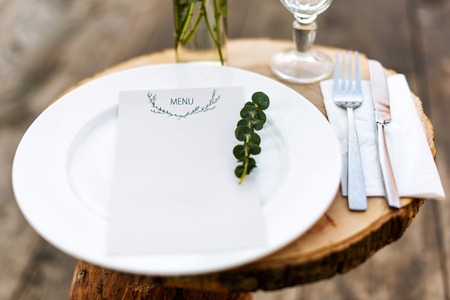 Paper menu on decorated table ready for dinner. Beautifully decorated table set with flowers, plates and serviettes for outdoor wedding ceremony or another event in the restaurant. Selective focusの写真素材