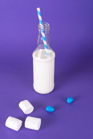 Milk cocktail with retro cocktail tube, served in bottle on colorful background with sweet marshmallowsの写真素材