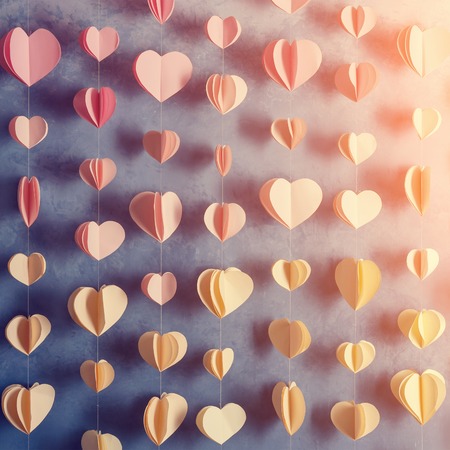 Colorful hearts paper garland hanging on the wall. Romantic Valentine's day background. Instagram style toned photoの写真素材