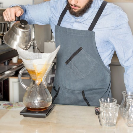 Barista making kemeks coffee. Man with a beard pours boiling water into the filter with ground...