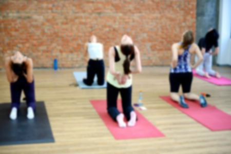 Blurred image of young women doing yoga indoors. Group workout in yoga studio. Selective focus