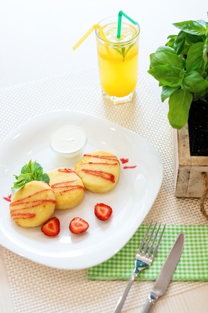 Cheese cookies with strawberry sauce, mint leaves on white plate and glass of lemon cold drink in restaurantの写真素材