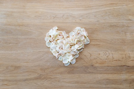 Heart made of white rose petals. Tea rose petals heart over wooden table. Top view with copy space for your text. Love and romantic themeの写真素材