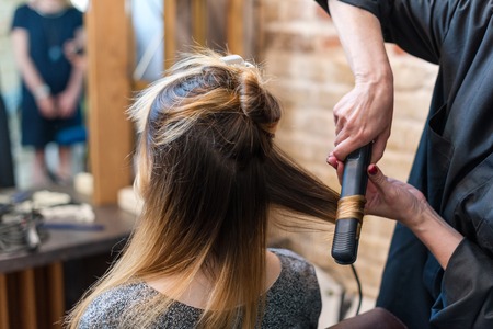 Professional hairdresser using curling iron. Hair curls in salon, people at workの写真素材