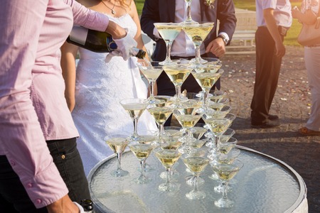 Waiter filling a pyramid of glasses with champagne at outdoor garden in wedding ceremony