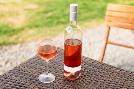 One glass and bottle of red or rose wine in autumn vineyard on wooden wicker table. Harvest time, picnic or wine fest themeの写真素材